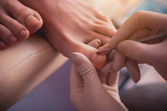 Close up woman hands polishing nails on leg of girl with special silver stick. Beauty salon concept
