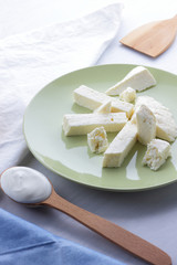Cheese and sour cream, feta in a green plate, soft cheese on a white background, wooden spoon with sour cream, French breakfast, blue napkin, dairy products on a light background, copy space