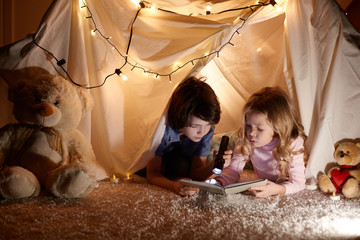 Little kids involving in reading amazing book. They lying in nice toy tent in playroom. Boy holding...