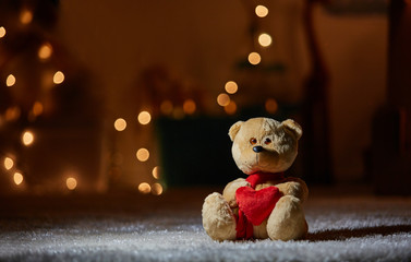 Focus on plush bear in nice red scarf holding soft heart. It is sitting on the floor. Copy space