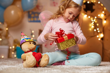 Cheerful child holding present in hands and trying open box. Involved kid sitting on carpet in playroom at home