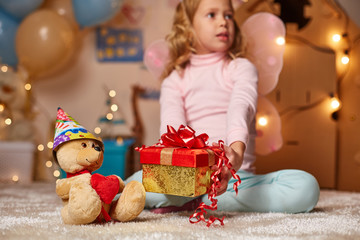 Little child sitting on carpet with present box and toys. She is looking away