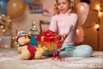 Fototapeta na wymiar Happy smiling kid presenting nice gift to toy bear in birthday cap. Concept of childhood
