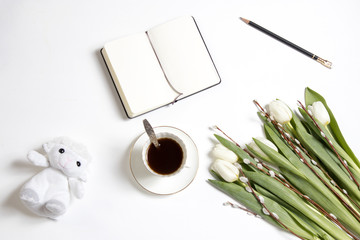 A cup of coffee with a notebook and a bouquet of white tulips on a wooden table