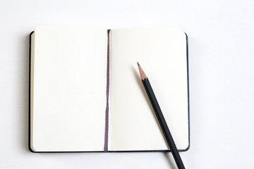 a white notebook and a black pencil on a white wooden table.