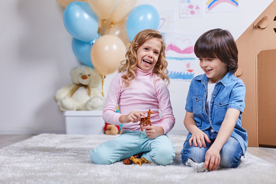 Portrait of cherfull children sitting on carpet and toying in game room. They playing with small figures of wild animals