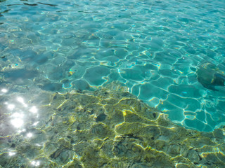 Fototapeta na wymiar Crystal turquoise water with twinkling and reflecting sunlight and stones on seabed