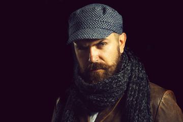 Advertise autumn-winter fashion. Serious man with beard and mustache in warm scarf wrapped around his neck, hat on head and leather jacket. Copy space for advertise clothing store.