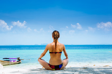 Young woman doing yoga exercises on the sea beach