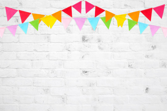 Colorful party flags hanging on white brick wall  background, birthday, anniversary, celebrate event, festival greeting card background