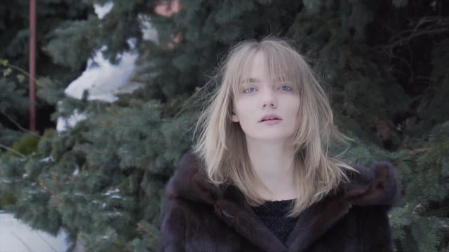 pretty woman in fur coat wearing a hood goes away in snowy winter forest