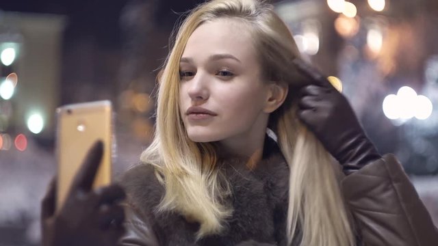 Happy young woman doing a selfie outdoor in night. beautiful smiling girl. Beautiful young woman taking selfie in the city