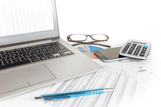finance calculation with laptop, glasses, pen and calculator lying on printed number charts on a white office desk, business concept, copy space