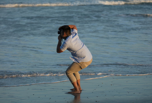 unknown male photographer taking pictures on the beach at sunset