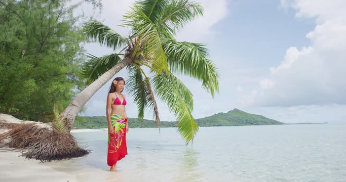 Vacation travel woman relaxing on paradise beach on holidays on a motu Beach, Bora Bora. Happy girl on holidays beach vacation wearing traditional pareo in Tahiti, French Polynesia. SLOW MOTION.