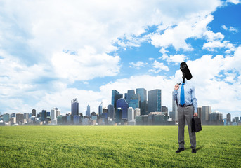 Camera headed man standing on green grass against modern cityscape