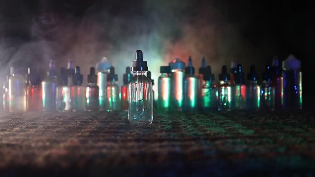 Vape concept. Slider shot. Smoke clouds and vape liquid bottles on dark background. Light effects. Useful as background or vape advertisement. Selective focus