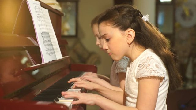 Cheerful beautiful small girls play piano together
