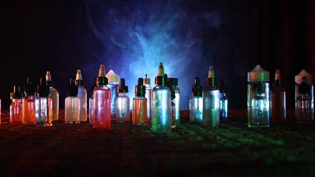 Vape concept. Slider shot. Smoke clouds and vape liquid bottles on dark background. Light effects. Useful as background or vape advertisement. Selective focus