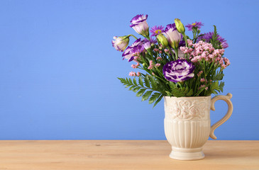 summer bouquet of purple flowers in the vase over wooden table and blue background.