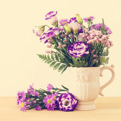 summer bouquet of purple flowers in the vase over wooden table and white background.