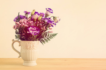 summer bouquet of purple flowers in the vase over wooden table and white background.