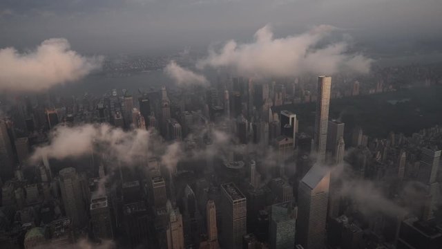 New York City aerial view flying over Midtown Manhattan skyscrapers and the Upper East Side under low level clouds at sunrise.