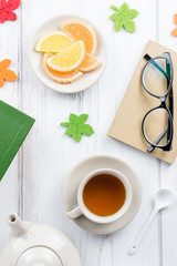 Feminine desk workspace flat lay with diary, eyeglasses, book, tea mug, sweets and felt decor.