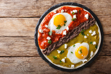 Mexican breakfast: eggs huevos divorciados with beans Frijoles refritos, two sauces roja and verde and cheese Queso Fresco close-up. horizontal top view