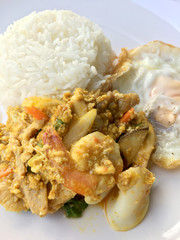 Stir fry prawns and squid with curry power thai style with fried egg with rice in white dish on black fabric texture background. Thai style food.