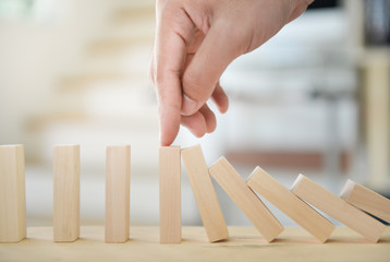 Man hand is holding the wooden block of tumbling tower to stop falling for business concept