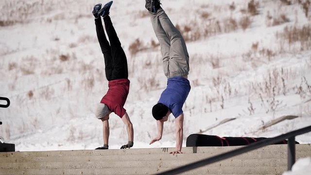 Two athletic man going downstairs doing a handstand outdoor in winter.