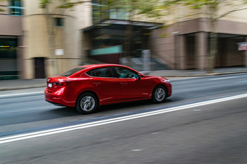 Fototapeta na wymiar Red car in motion on the road, Sydney, Australia. Car moving on the road, blurred buildings in background.