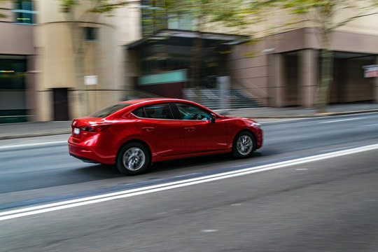 Fototapeta Red car in motion on the road, Sydney, Australia. Car moving on the road, blurred buildings in background.