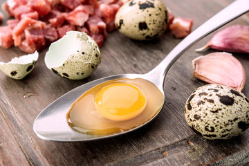Raw eggs and open quail in metal spoon, on rustic wood