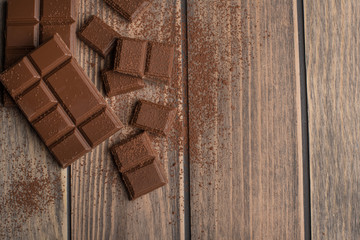 Milk chocolate with cocoa powder. Top view, on a wooden texture. C blank space for inscription or advertising.