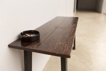 Black Ashtray with cigarette butt on the table by the wall.