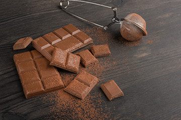 Milk chocolate with cocoa powder. On a wooden texture. C blank space for inscription or advertising.