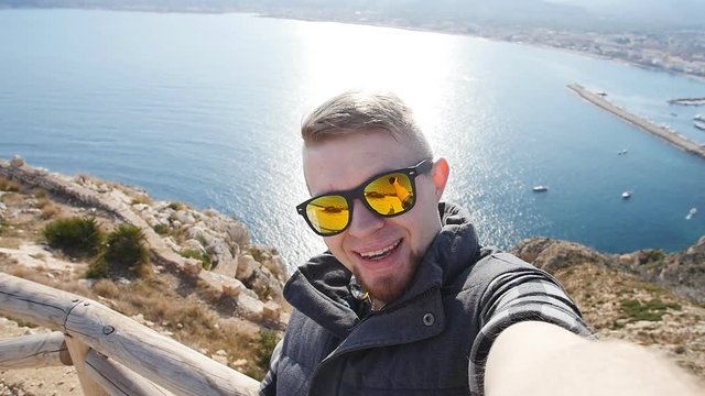 Young man taking travel selfie on trekking excursion day. Against the background of the sea and rocks