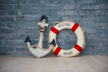A composition on a sea theme with an anchor and life ring on a gray brick wall.