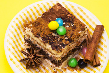 delicious portion of tiramisu with candies and cinnamon on yellow background