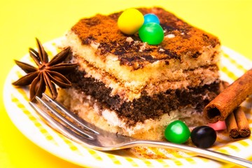 delicious portion of tiramisu with candies and cinnamon on yellow background