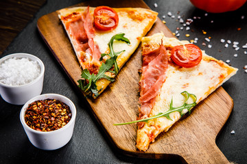 Slices of pizza with ham and vegetables on wooden table