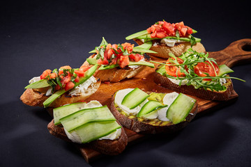 Grilled toast brisket with tomato, avocado and ruccola over dark background, top view, close-up, selective focus