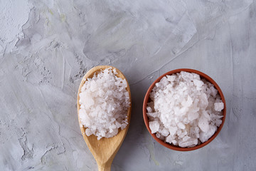 Composition of sea salt in ceramic bowl and spoon for cooking or spa on white background, top view, selective focus