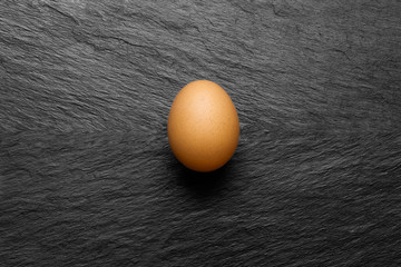 One Chicken Egg on Black Stone Background Surface With Free Space