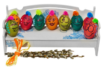 Easter eggs painted in smiling cartoon faces are sitting on a wooden bench. Decorated eggs with funny colorful hairstyles.