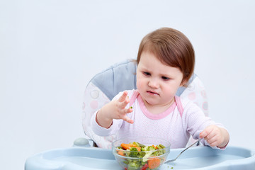 Obraz na płótnie Canvas Adorable toddler girl is having fun while eating stewed vegetables on white background