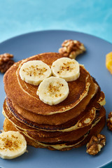 Pile of homemade pancakes with banana and walnuts on blue background, selective focus