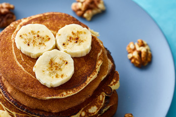 Pile of homemade pancakes with banana and walnuts on blue background, selective focus